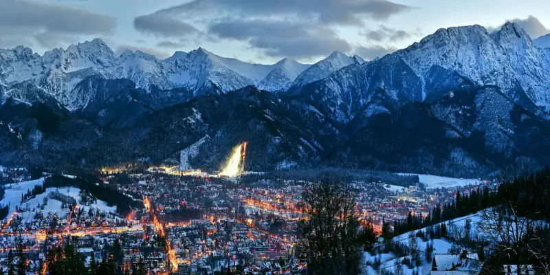 Oświetlone miasto Zakopane nocą, otoczone ośnieżonymi górami. Idealne miejsce na zakup biletów na zimowy wypoczynek.