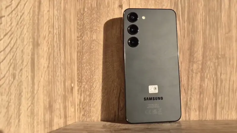 Szary Samsung S23 z trzema obiektywami aparatu na drewnianym tle. Długo działająca bateria pozwoli Ci cieszyć się nim przez cały dzień.