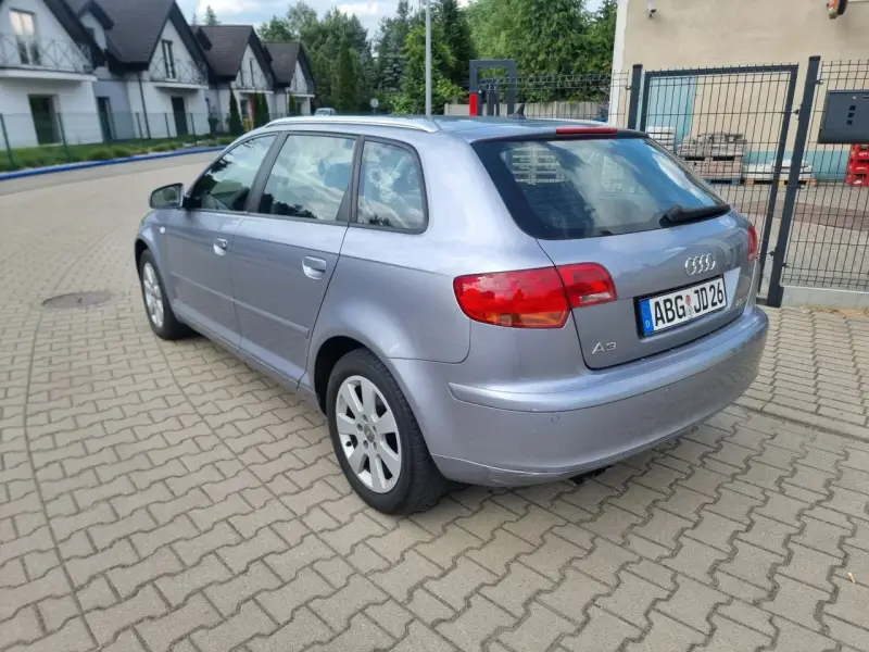 Srebrny Audi A3 kombi zaparkowany na kostce brukowej, w tle domy i drzewa.