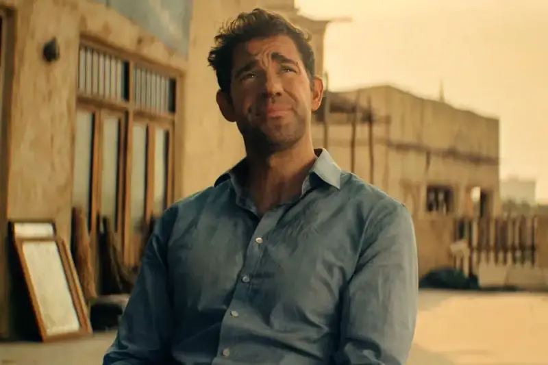 John Krasinski w niebieskiej koszuli, zamyślony. Widzimy fragmenty jego filmów, seriali i programów.