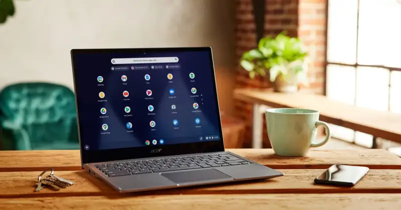 Laptop z systemem Chrome OS Flex na drewnianym stole, obok kubek i klucze.