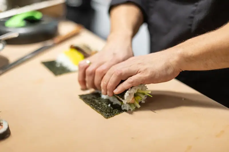 Ręce zwijają sushi na nori. Zastanawiasz się, nori gdzie kupić? W sklepach z azjatycką żywnością lub online.