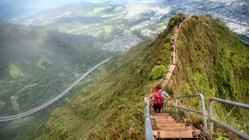 Wanderer erklimmen die "Stairway to Heaven" in Hawaii, eine steile Treppe mit atemberaubendem Blick auf die Stadt und die Natur.
