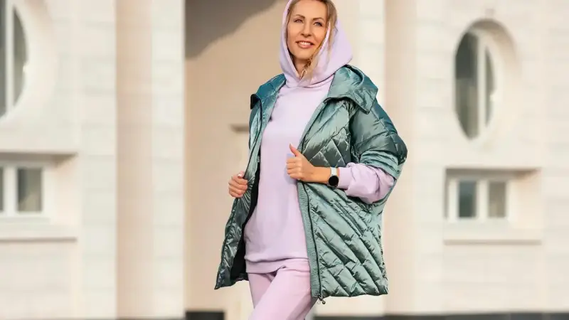 Uśmiechnięta kobieta w pastelowym komplecie dresy z wysokim stanem damskie i błyszczącej kurtce.