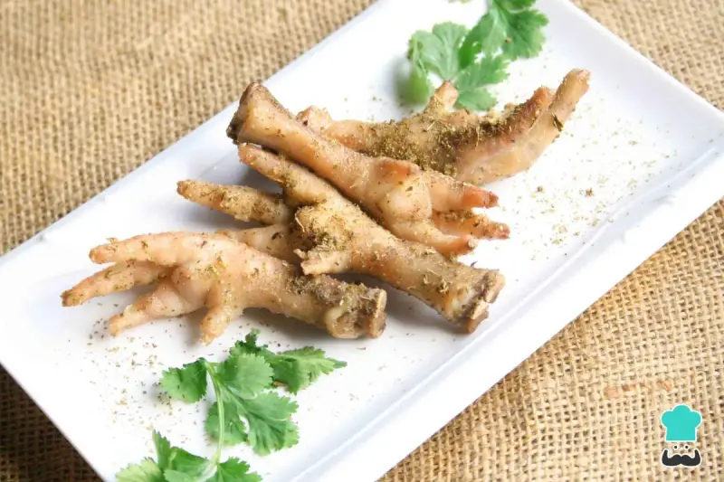 Patas de pollo sazonadas y listas para cocinar, adornadas con cilantro fresco sobre un plato blanco.