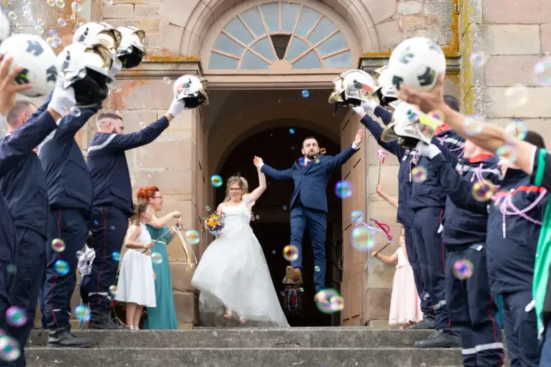 Mariés sortant de l'église sous une haie d'honneur mariage de pompiers lançant des bulles.