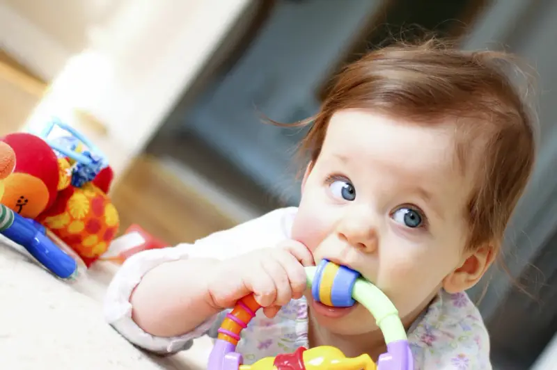 Bébé curieux mordillant un jouet coloré, dans le cadre d'un projet d'accueil individualisé pour son développement.