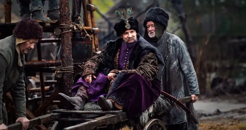 Bogaty pan w purpurowym stroju i futrzanej czapie z pawim piórem, siedzi na wozie. Czy to zapowiedź drugiego sezonu 1670?