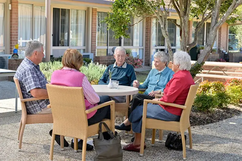 Anziani riuniti in giardino, chiacchierano e sorridono. Un momento sereno nella loro casa di riposo RSA.