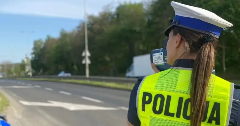 Policjantka w kamizelce odblaskowej mierzy prędkość pojazdów. Uważaj na tryb przyspieszony na drodze!