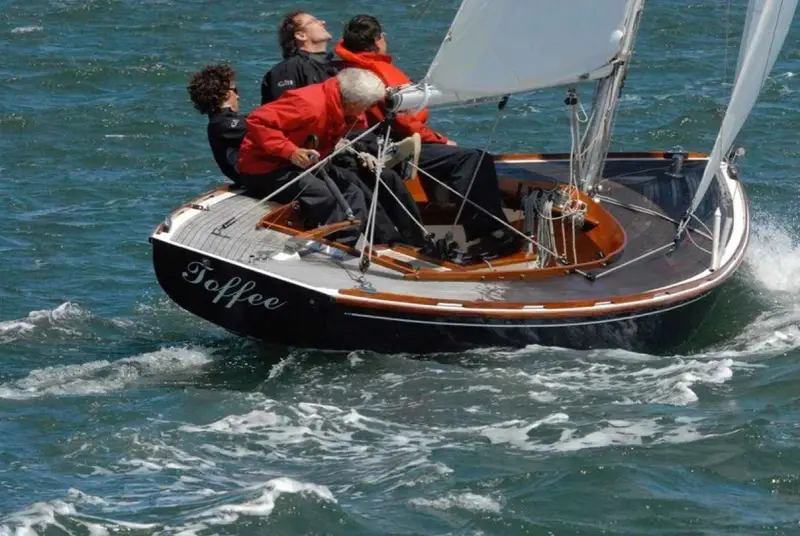 Le voilier "Toffee" navigue sur une mer agitée, quatre personnes à bord profitent de la balade.