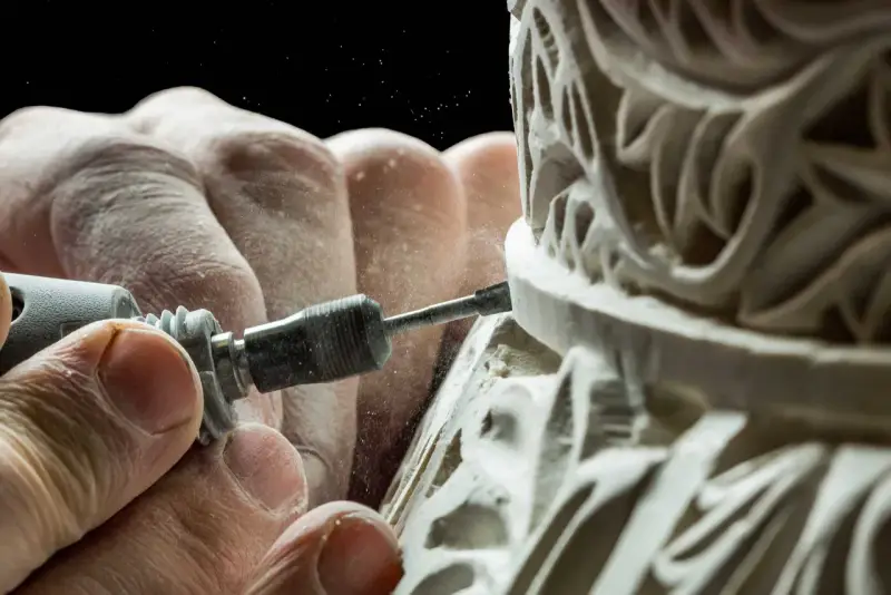Mains habiles sculptant un ornement complexe, poussière fine dans l'air. Une image capturant la précision de la formation artisanat d'art.