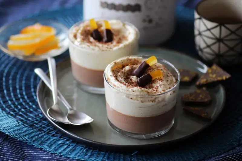 Deux verrines 3 chocolat, garnies de crème fouettée, de copeaux de chocolat et d'écorces d'orange confites.