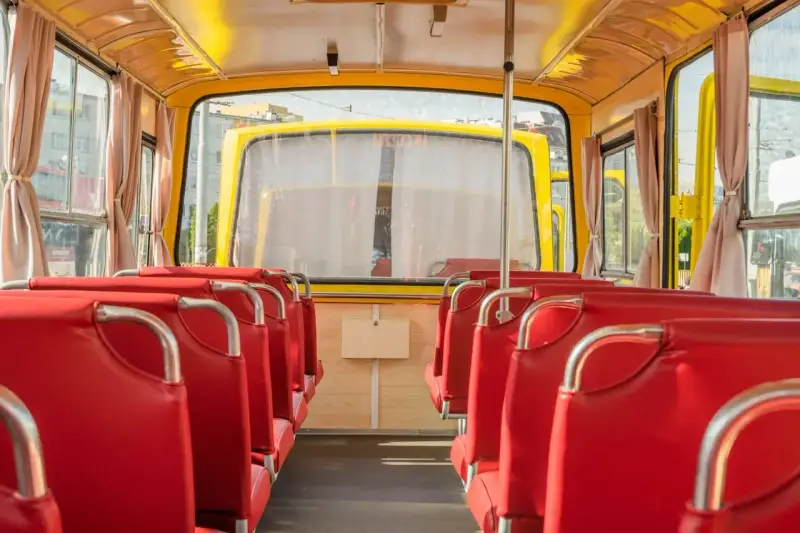 Wnętrze żółtego autobusu z czerwonymi siedzeniami, widok od tyłu.