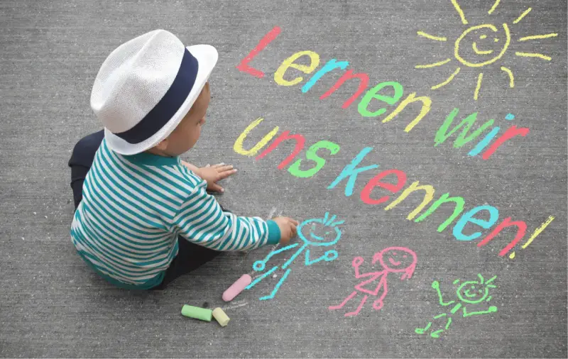 Kleiner Junge mit Hut malt mit Kreide auf Asphalt. Namensspiele für Kinder: "Lernen wir uns kennen!" mit Sonne und Figuren.