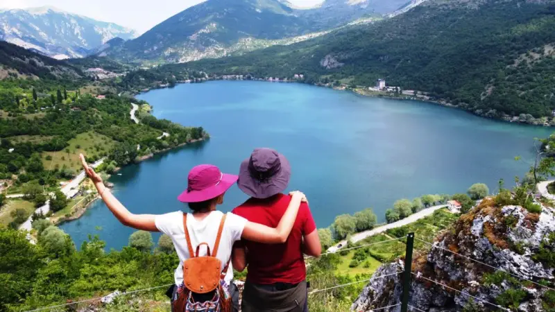 Coppia ammira un lago a forma di cuore, circondato da montagne verdi e alberi.
