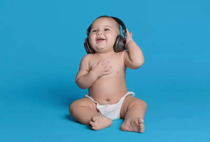 Un bébé souriant, en couche, écoute de la musique avec des écouteurs, le décibel maximum pour un bébé est à éviter.