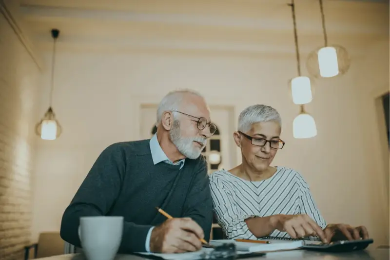 Couple âgé discutant de la différence entre article 82 et 83, l'un écrit, l'autre utilise une calculatrice.