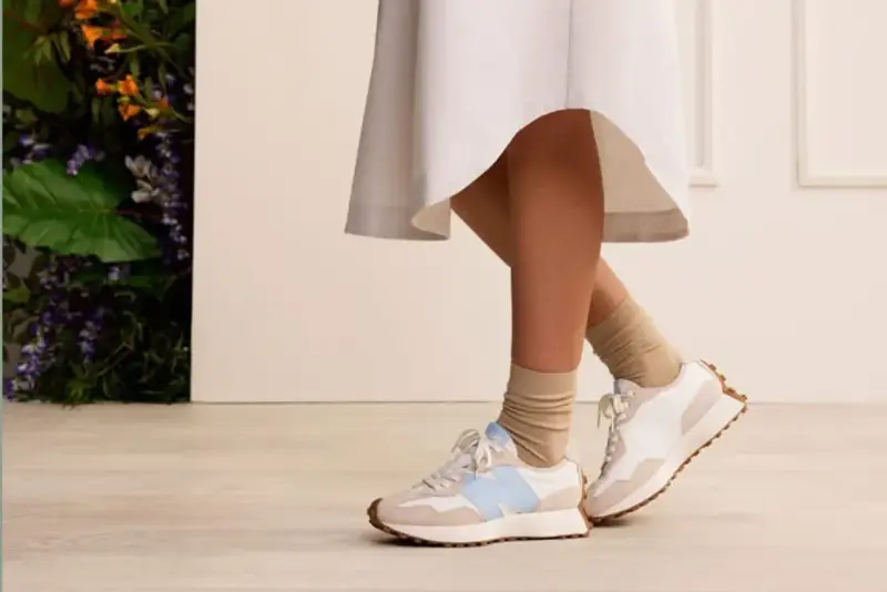 Elegancka sukienka i sportowe buty tworzą stylowy kontrast. Nogi w beżowych skarpetkach i białych sneakersach z błękitnym logo.