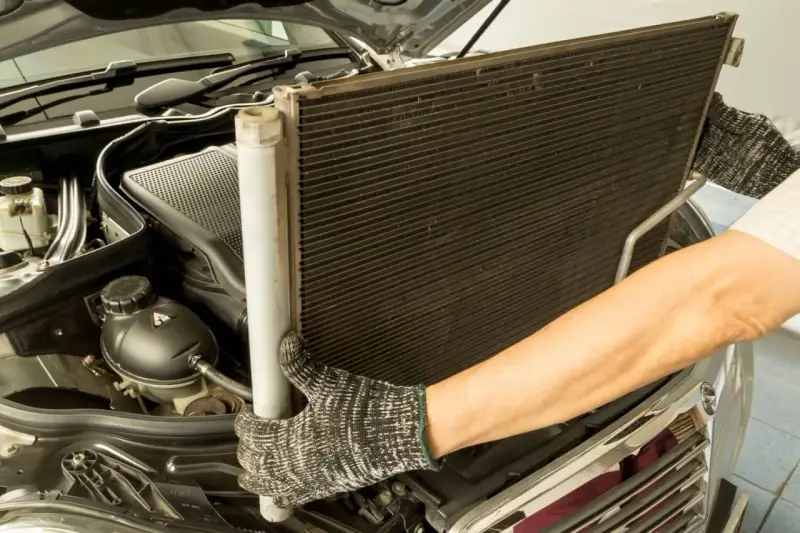 Mechanik w rękawicach wyjmuje chłodnicę klimatyzacji z silnika samochodu.