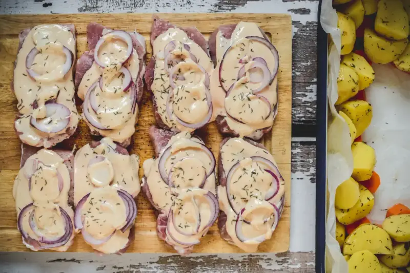 Schab pieczony w plastrach, polany kremowym sosem i posypany ziołami, obok pieczone ziemniaki.