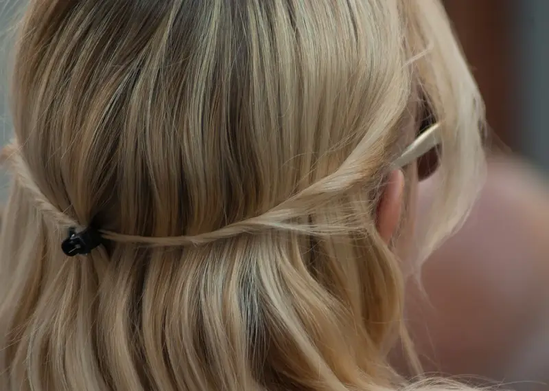 Piaskowy blond włosów spięty warkoczem z tyłu głowy. Delikatne pasma opadają na ramiona.