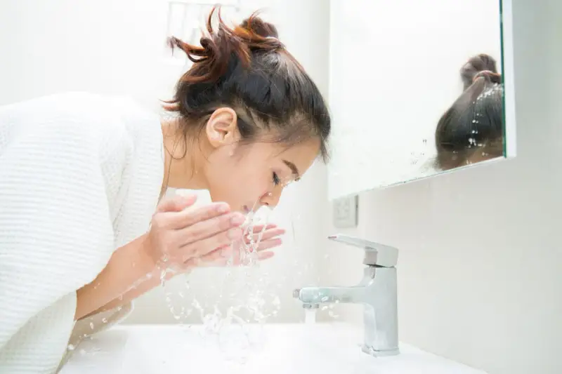 Une jeune femme se lave le visage le matin, sous un jet d'eau fraîche. Une routine beauté essentielle pour se réveiller.
