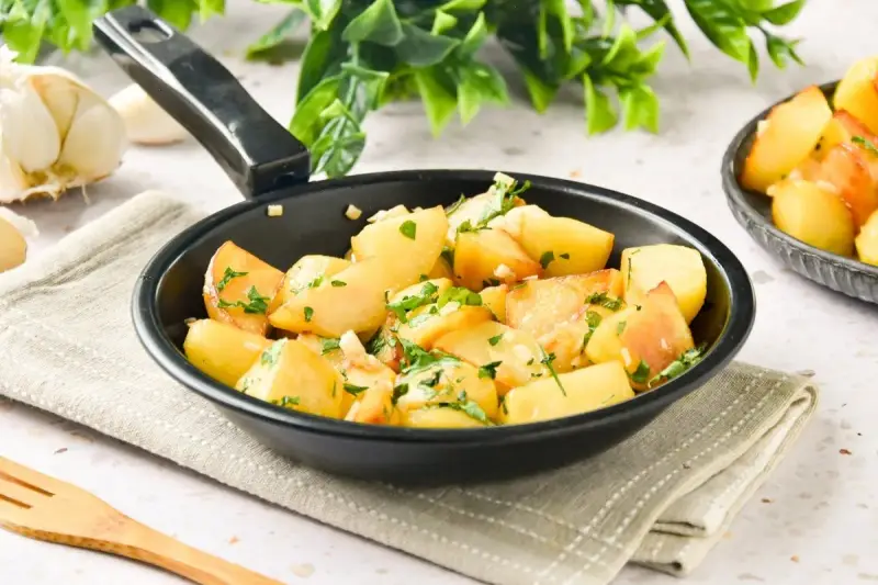 Patatas al ajillo recién hechas en sartén, con perejil fresco y ajos picados. ¡Un plato sencillo y delicioso!