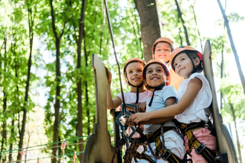 Quatre enfants souriants portant des casques de sécurité dans un parc d'aventure.