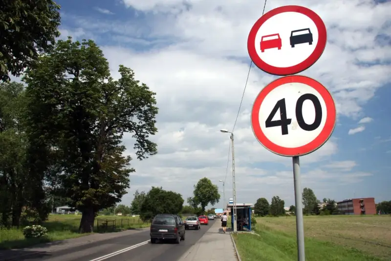 Znaki drogowe: zakaz wyprzedzania i ograniczenie prędkości do 40 km/h. Droga z samochodami i drzewami.