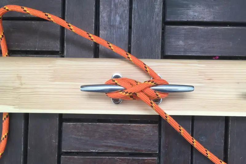 Pomarańczowa lina z żółtymi i czarnymi paskami tworzy solidny knaga węzeł na metalowym knadze.