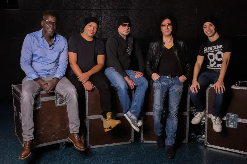 Les membres de Trust (groupe) posent ensemble, assis sur des flight cases, prêts pour leur prochaine performance.