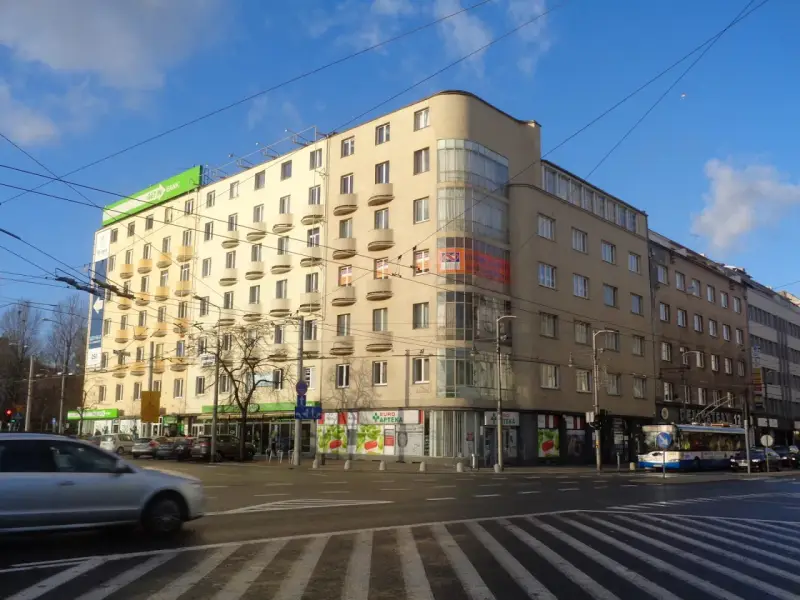 Charakterystyczny budynek z balkonami i zaokrąglonym narożnikiem, przykład modernizmu w architekturze, na tle błękitnego nieba.