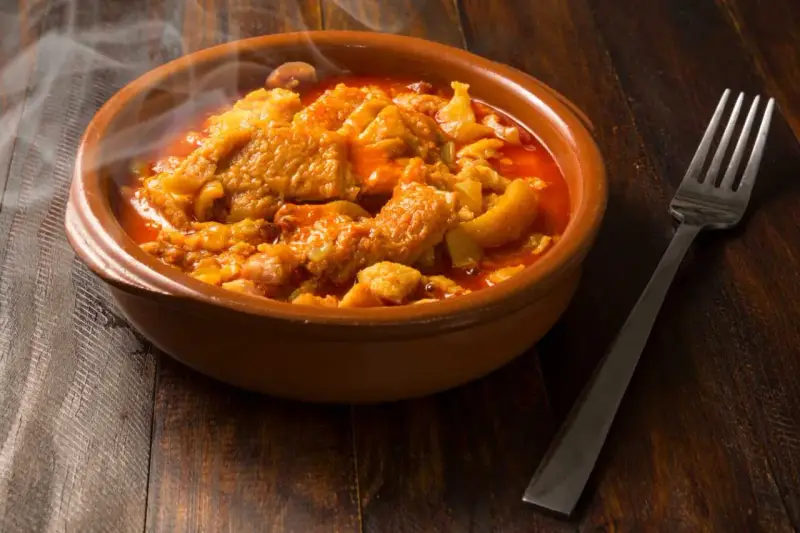 Un plat fumant de tête de veau mijotée, rappelant la recette tête de veau grand mère, servi dans un bol en terre cuite avec une fourchette.