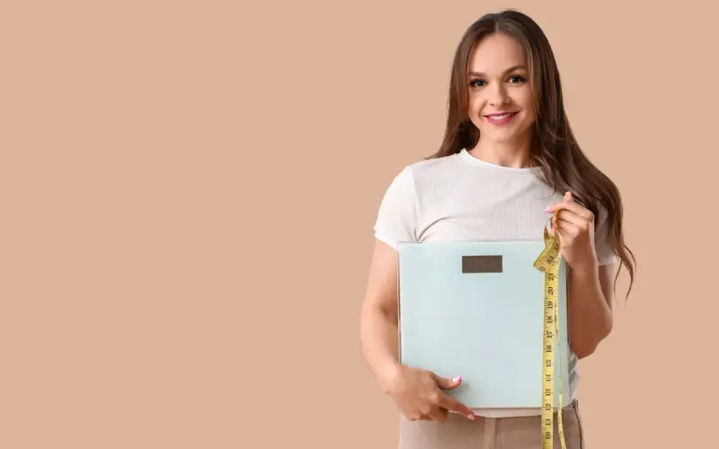 Femme souriante tenant une balance et un mètre ruban, prête à perdre 10 kilos.