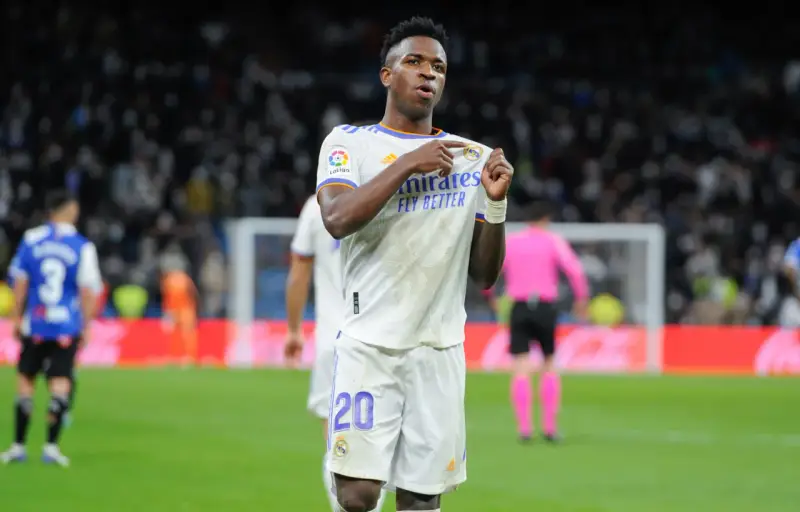 Vinicius Jr. w białej koszulce Realu Madryt z numerem 20, świętuje bramkę na tle trybun.