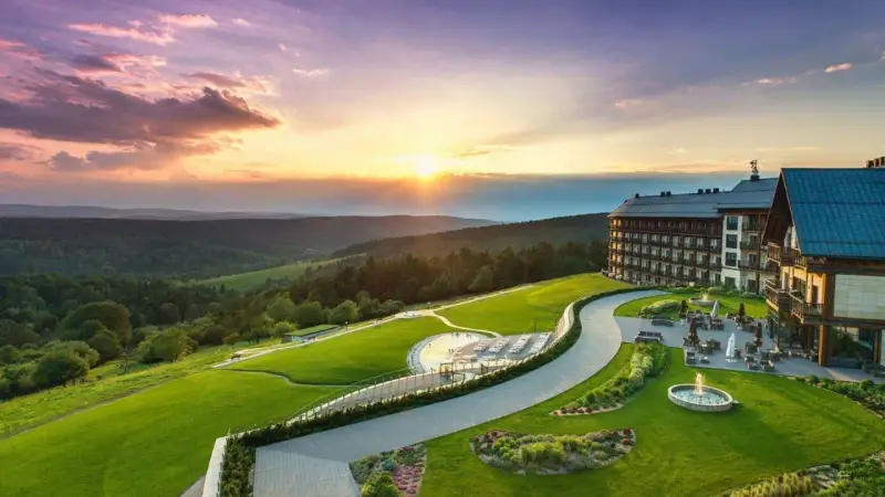 Hotel Arłamów z basenem i tarasem, otoczony zielonymi wzgórzami o zachodzie słońca. Ile pokoi ma hotel Arłamów? Tego nie widać, ale jest ich wiele!