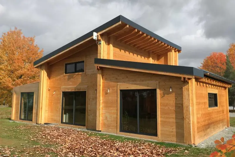 Une belle maison en bois, prête à accueillir ses habitants. L'automne arrive, les feuilles tombent autour de cette construction chaleureuse.