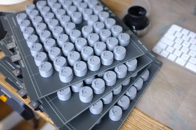 Stosy szarych, cylindrycznych elementów, świeżo po prototypowaniu 3d. Obok klawiatura i kałamarz.
