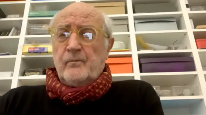Ritratto di Francesco Pecoraro con occhiali gialli e sciarpa rossa, davanti a una libreria piena di scatole.