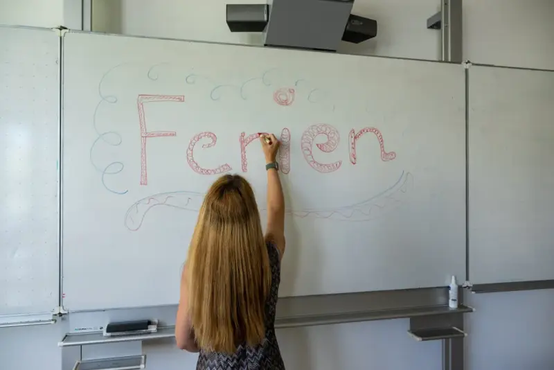 Frau schreibt "Ferien" an Tafel, Vorfreude auf Pfingstferien Rheinland-Pfalz.