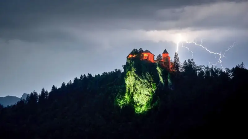 Zamek Poenari, oświetlony na czerwono, góruje nad skalistym zboczem podczas burzy z piorunami.