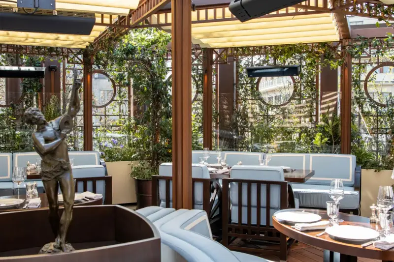 Terrazza lussuosa con statue e piante, tavoli apparecchiati per un'esperienza culinaria al **Wilde Milano**.