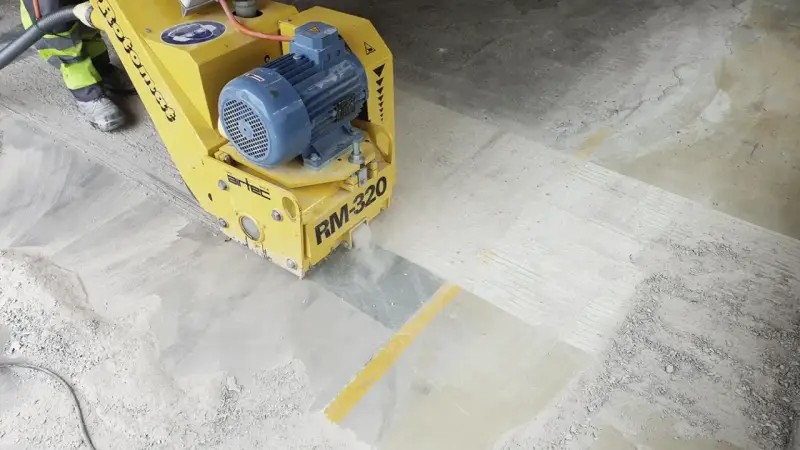 Żółta maszyna do szlifowania betonu RM-320 pracuje na posadzce, tworząc pył.