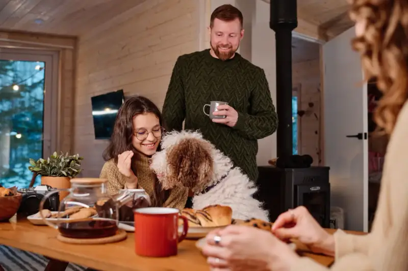 Familj med hund myser vid bordet med fika. Trots att det är lite dålig luft hemma, sprider sig värme och glädje.
