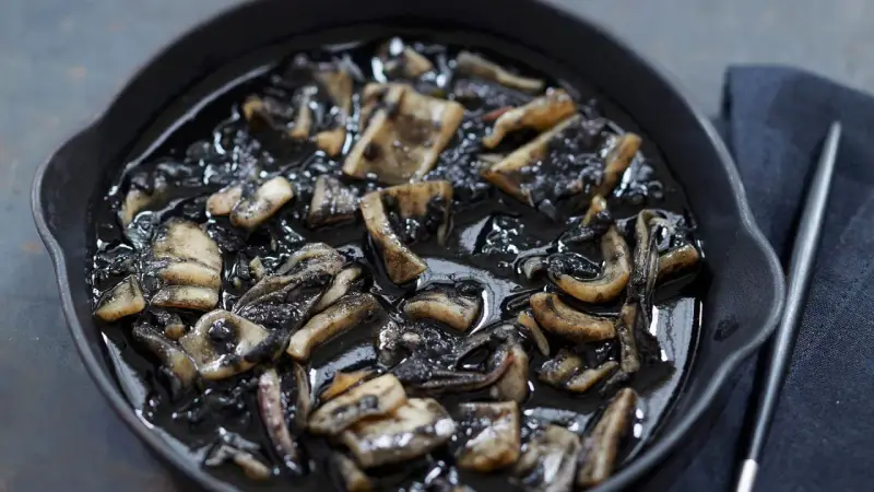 Calamares en su tinta, un plato oscuro y sabroso, servido en una sartén de hierro fundido.