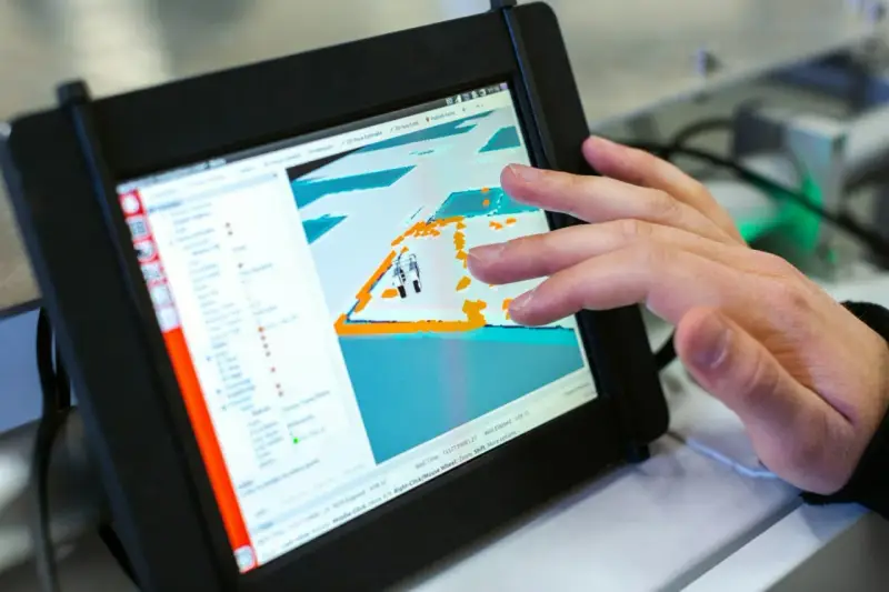Ein Finger tippt auf ein Tablet, das eine 3D-Ansicht mit einem Roboter zeigt. Die dji app windows wird zur Steuerung genutzt.