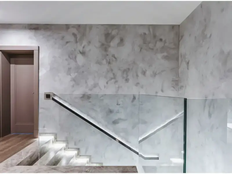Nowoczesny hol z podświetlanymi schodami i szklaną balustradą. Efektowny tynk na ścianie dodaje wnętrzu elegancji.