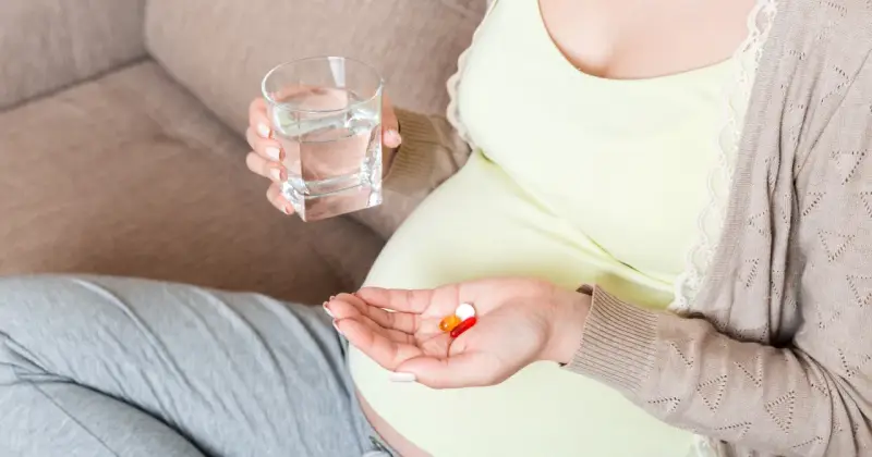 Kobieta w ciąży bierze suplementy, w tym magnez, popijając wodą. Dba o zdrowie swoje i dziecka.