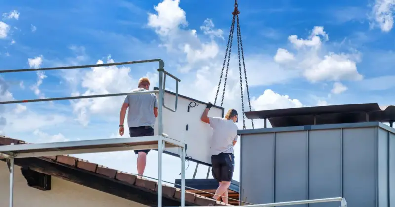 Dwaj pracownicy montują panel fotowoltaiczny na dachu. Ciężka praca i ryzyko wypadku to negatywne skutki fotowoltaiki, które często się pomija.